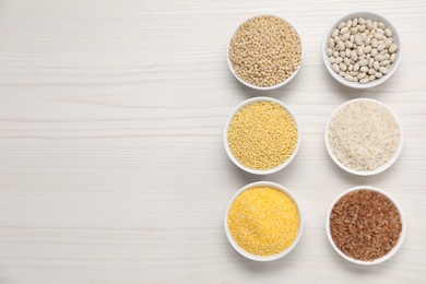 Photo of Different types of cereals and legumes in bowls on white wooden table, flat lay. Space for text