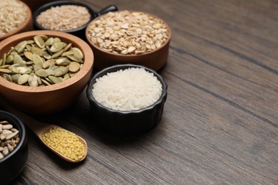 Different types of cereals and seeds on wooden table. Space for text