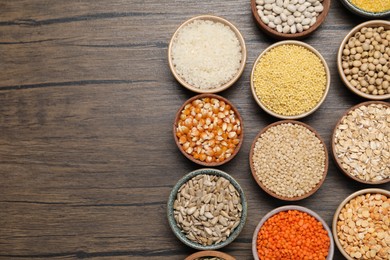 Different types of cereals, seeds and legumes in bowls on wooden table, flat lay. Space for text