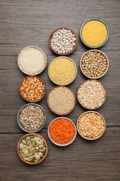 Photo of Different types of cereals, seeds and legumes in bowls on wooden table, flat lay