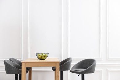 Photo of Bar stools and table near white wall. Space for text