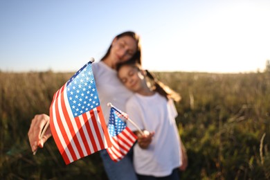 Photo of Mother and daughter with flags of USA outdoors, selective focus