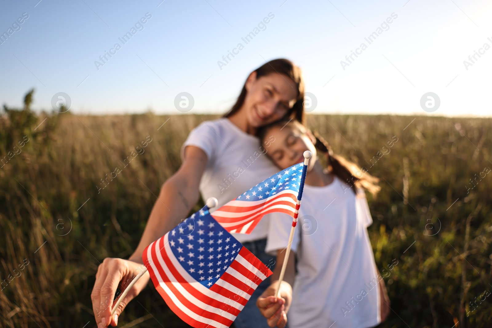 Photo of Mother and daughter with flags of USA outdoors, selective focus