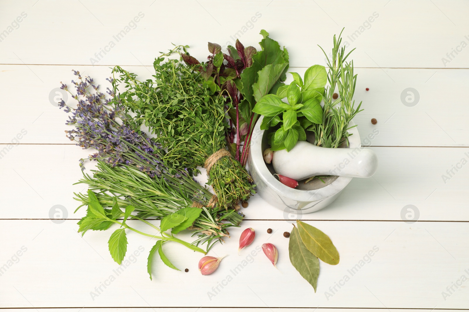 Photo of Different aromatic herbs, garlic, mortar and pestle on white wooden table, top view