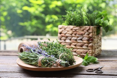 Photo of Different aromatic herbs and scissors on wooden table against blurred background