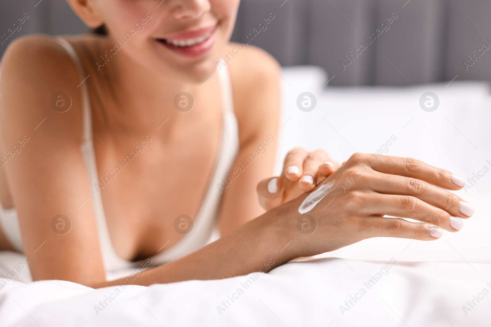 Photo of Smiling woman applying cream onto hand on bed, closeup. Body care