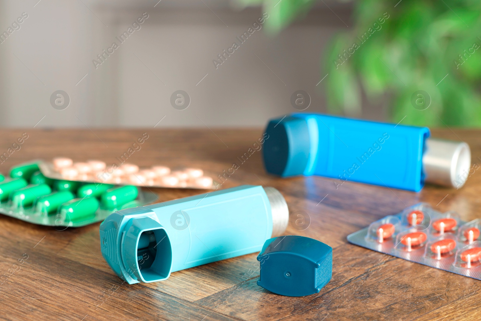 Photo of Inhalers and pills on wooden table indoors, closeup. Asthma treatment