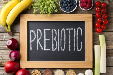 Photo of Chalkboard with word Prebiotic and different products on wooden table, flat lay