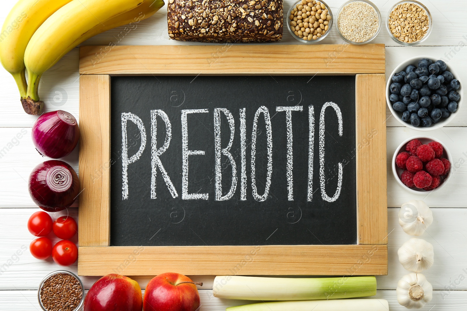 Photo of Chalkboard with word Prebiotic and different products on white wooden table, flat lay