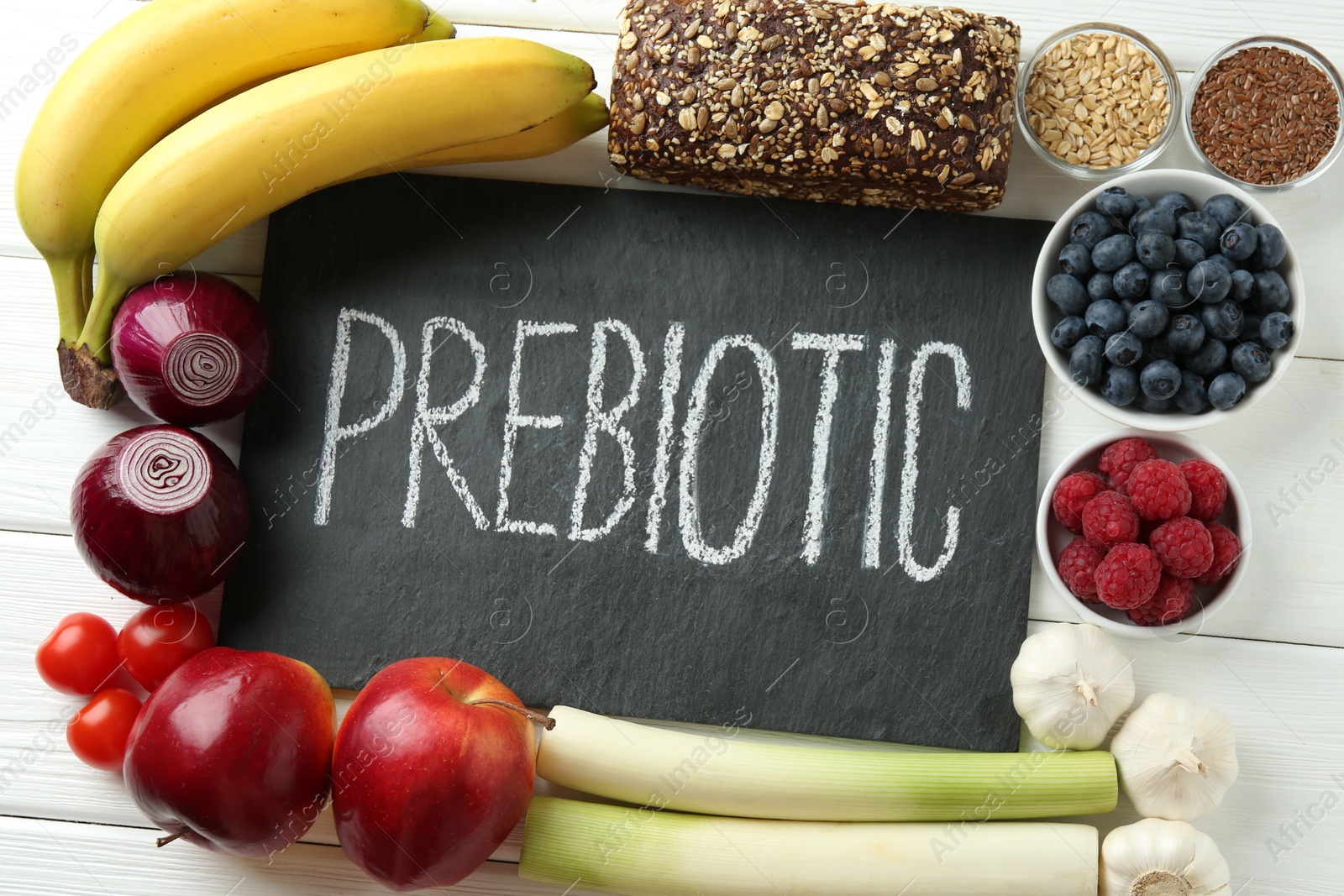 Photo of Slate board with word Prebiotic and different products on white wooden table, flat lay