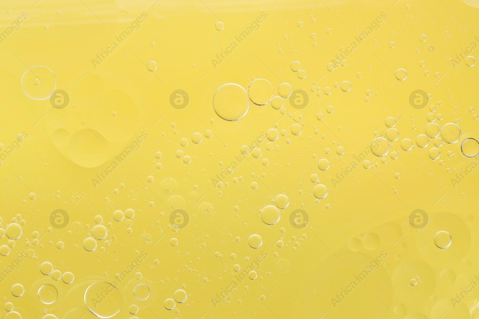 Photo of Essential oil bubbles on yellow background, macro view. Cosmetic product