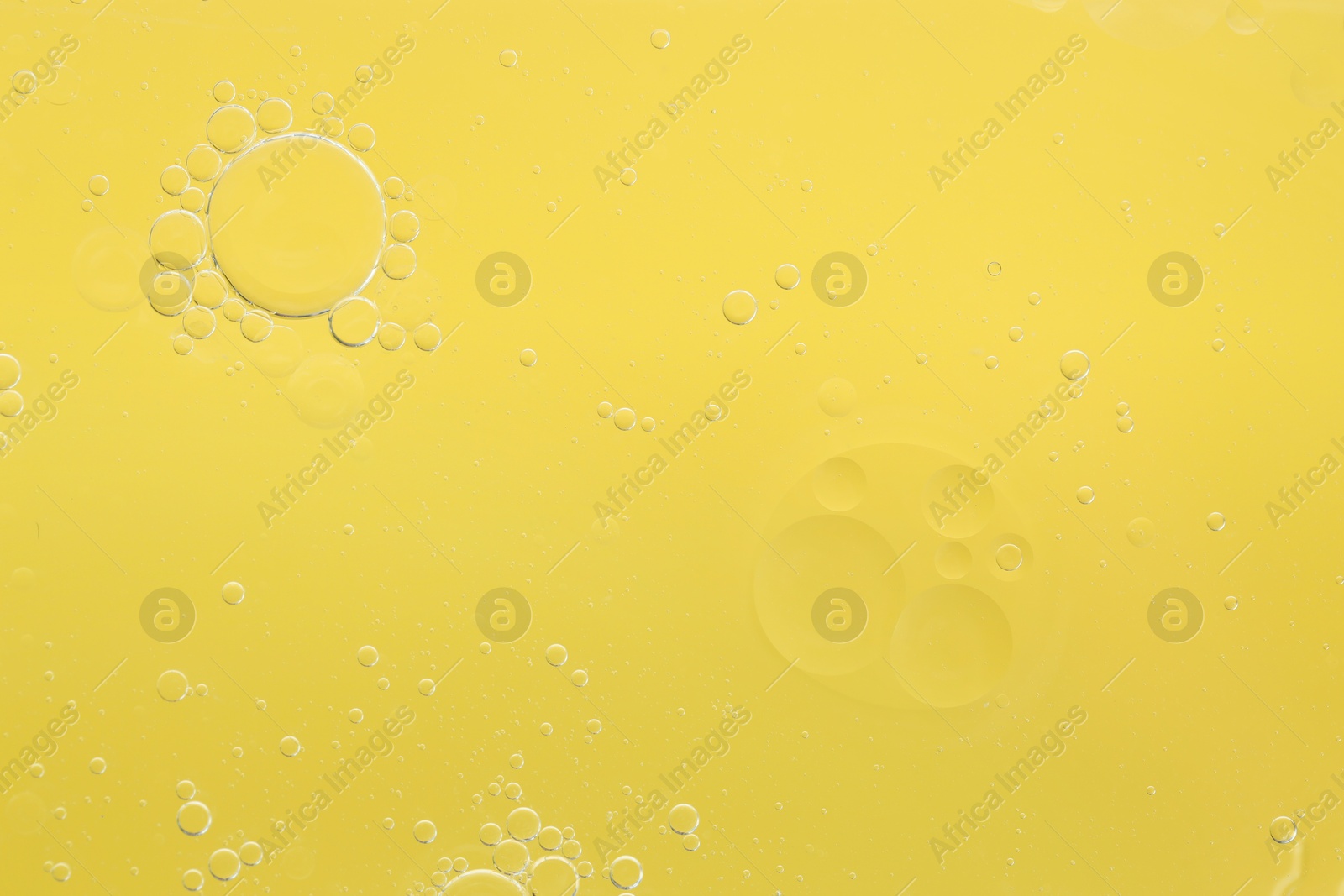 Photo of Essential oil bubbles on yellow background, macro view. Cosmetic product