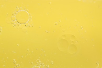 Photo of Essential oil bubbles on yellow background, macro view. Cosmetic product