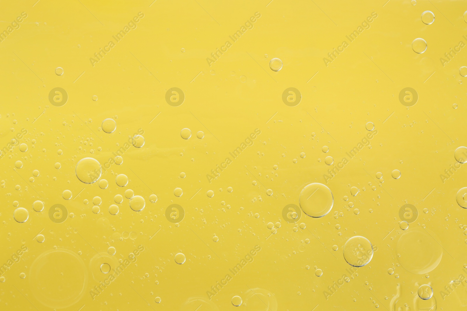 Photo of Essential oil bubbles on yellow background, macro view. Cosmetic product