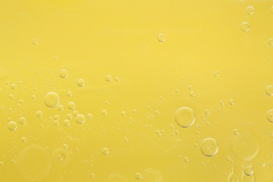 Photo of Essential oil bubbles on yellow background, macro view. Cosmetic product