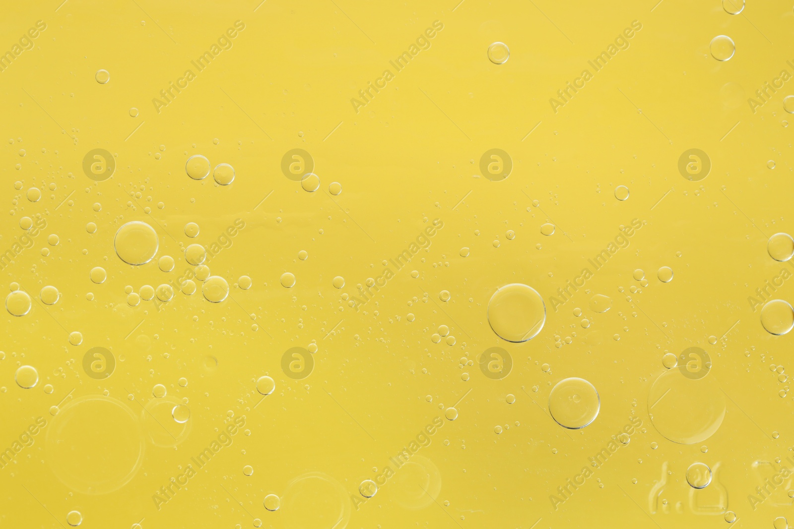 Photo of Essential oil bubbles on yellow background, macro view. Cosmetic product