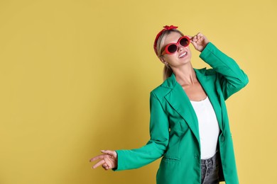 Beautiful woman in stylish green jacket on yellow background, space for text