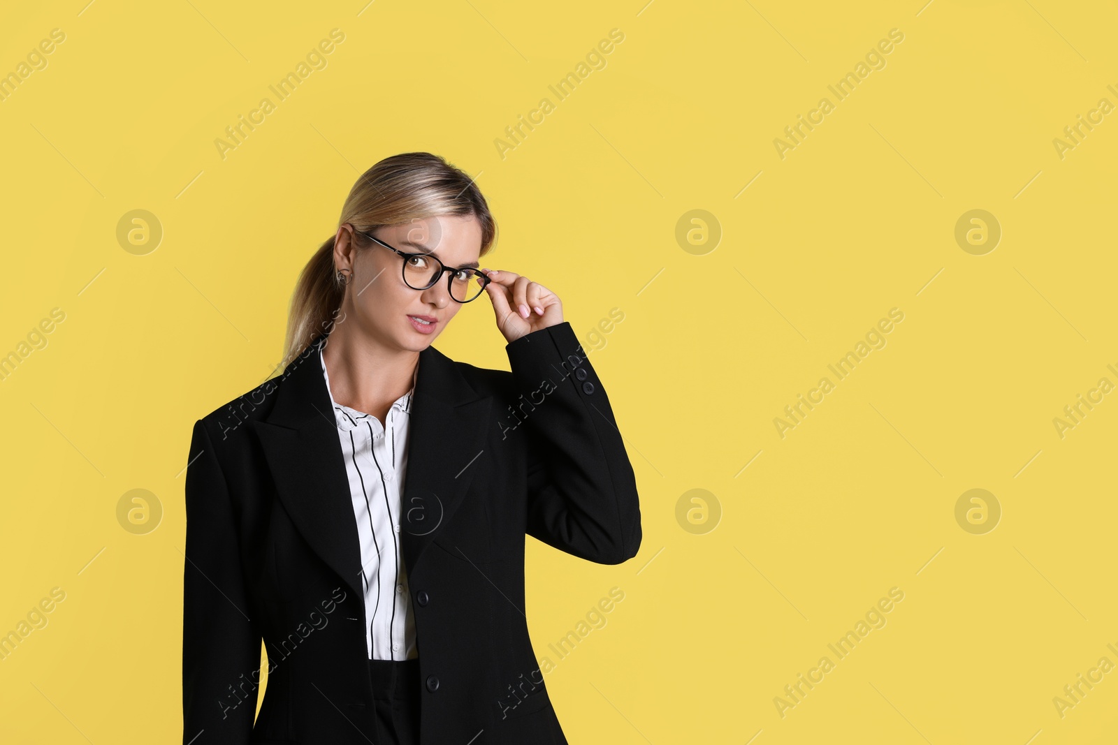 Photo of Beautiful woman in stylish black suit on yellow background, space for text