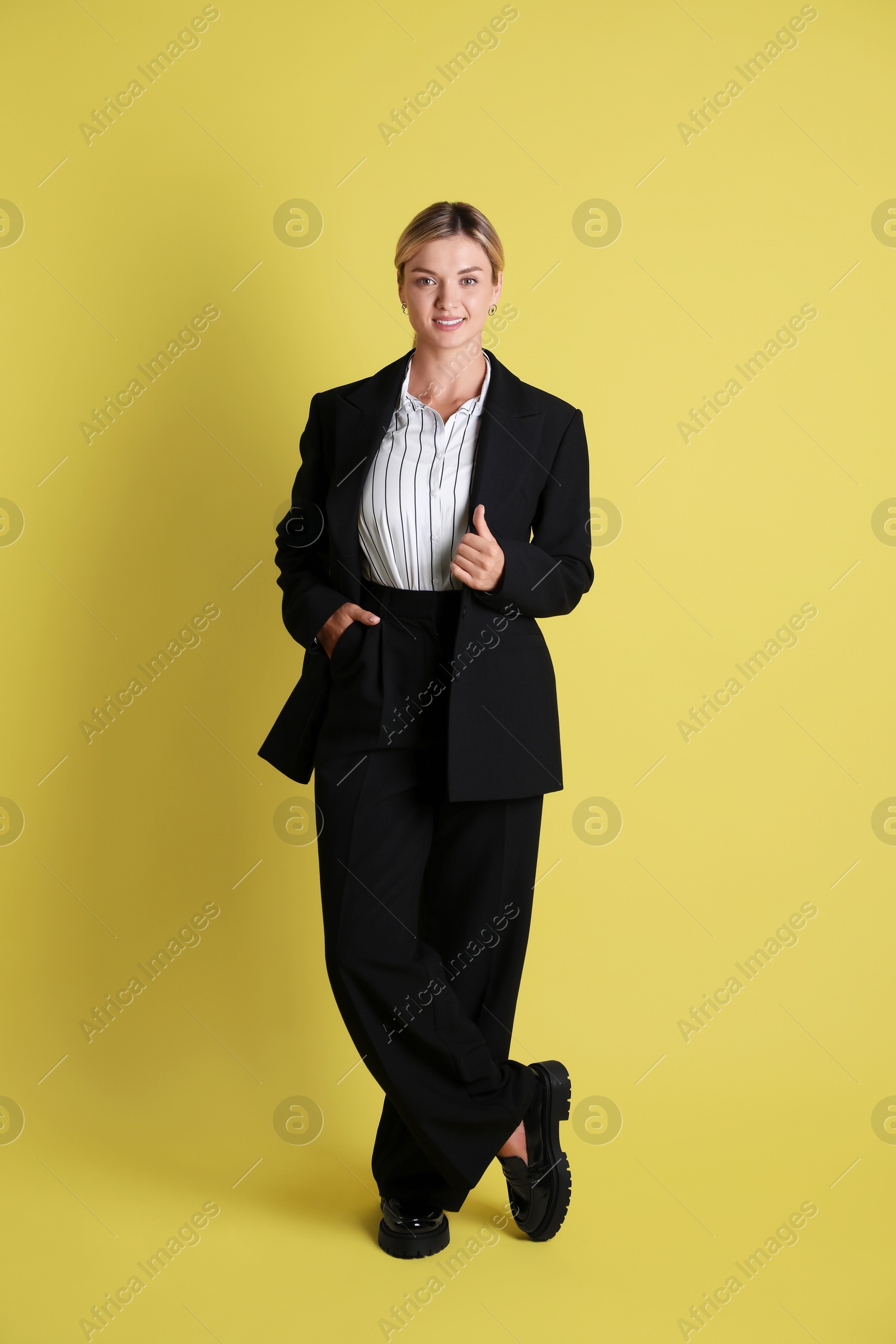 Photo of Beautiful woman in stylish black suit on yellow background