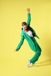 Beautiful woman in stylish green suit posing on yellow background