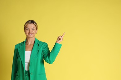 Photo of Beautiful woman in stylish green suit pointing at something on yellow background, space for text