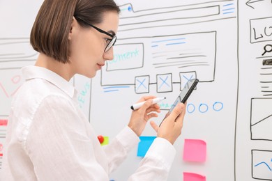 Developing UI design. Woman drawing website wireframe on whiteboard indoors