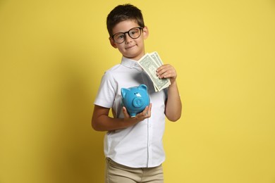 Photo of Cute boy with piggy bank and pocket money on yellow background