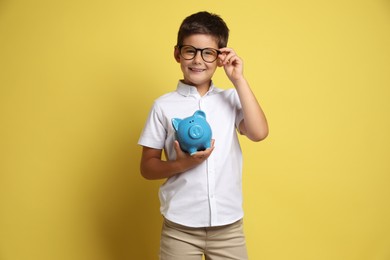 Photo of Pocket money. Cute boy with piggy bank on yellow background