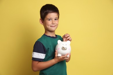 Photo of Pocket money. Cute boy with piggy bank and coins on yellow background