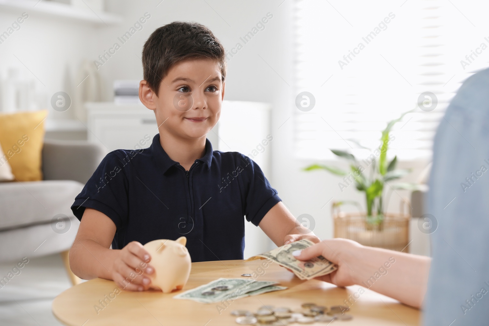 Photo of Mother giving pocket money to her son at table indoors