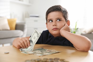 Photo of Cute boy with pocket money at wooden table indoors