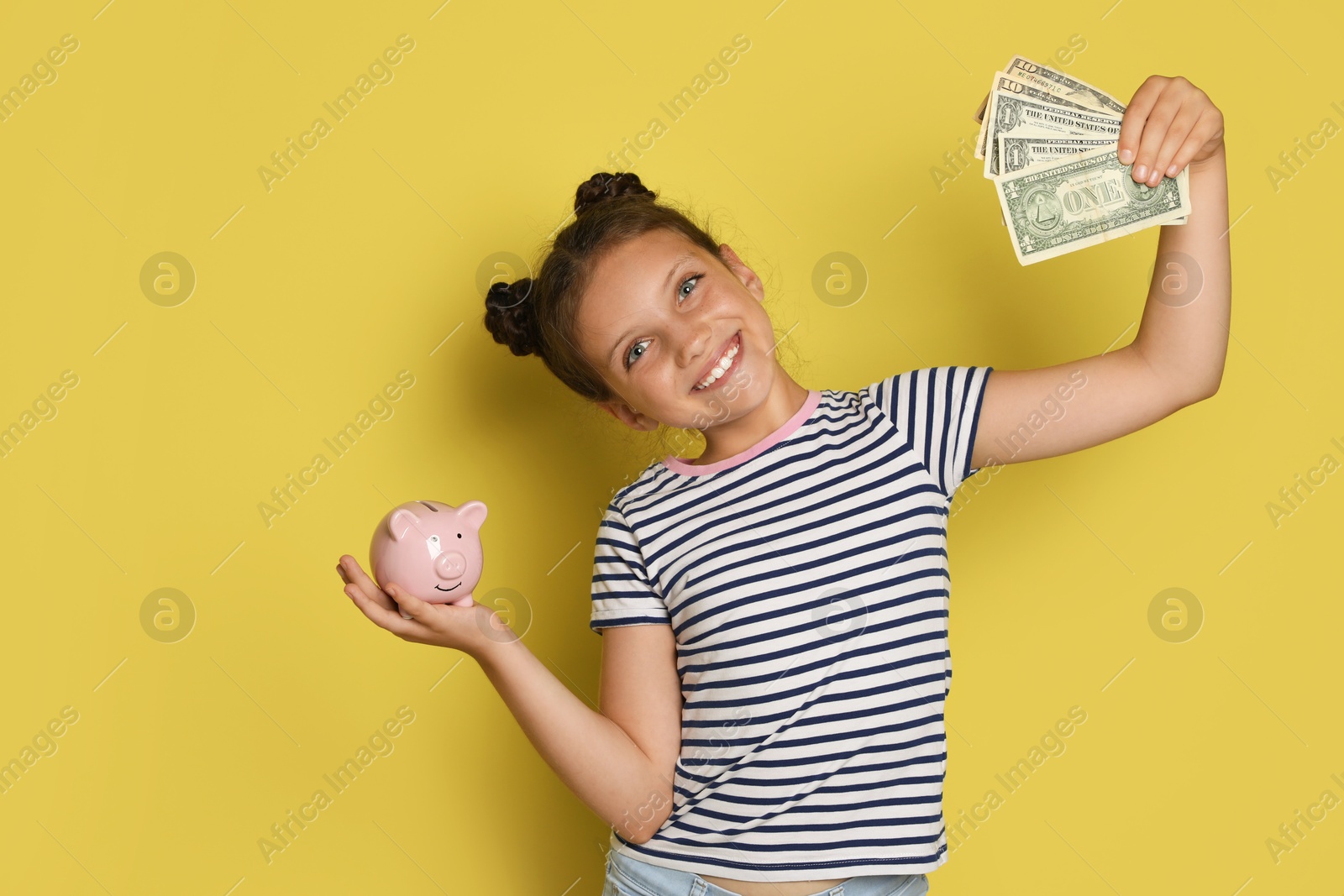 Photo of Pocket money. Cute girl with piggy bank and dollar banknotes on yellow background