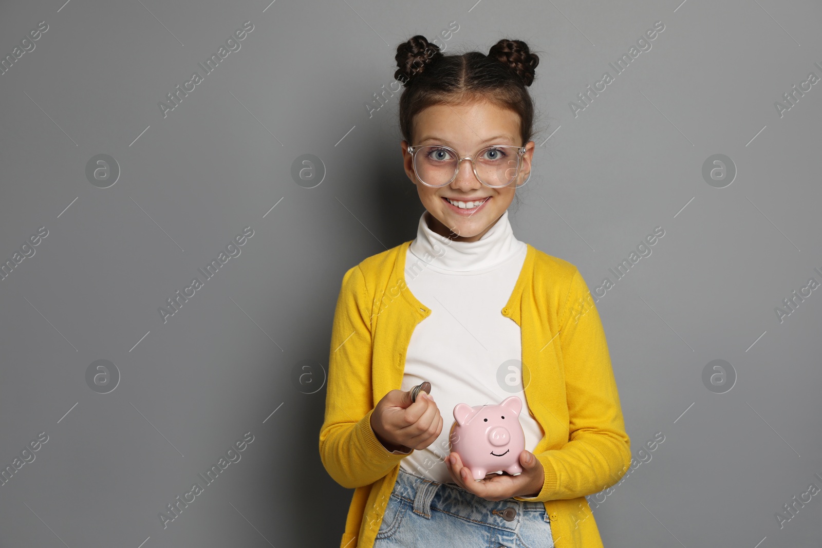 Photo of Pocket money. Cute girl with coins and piggy bank on grey background