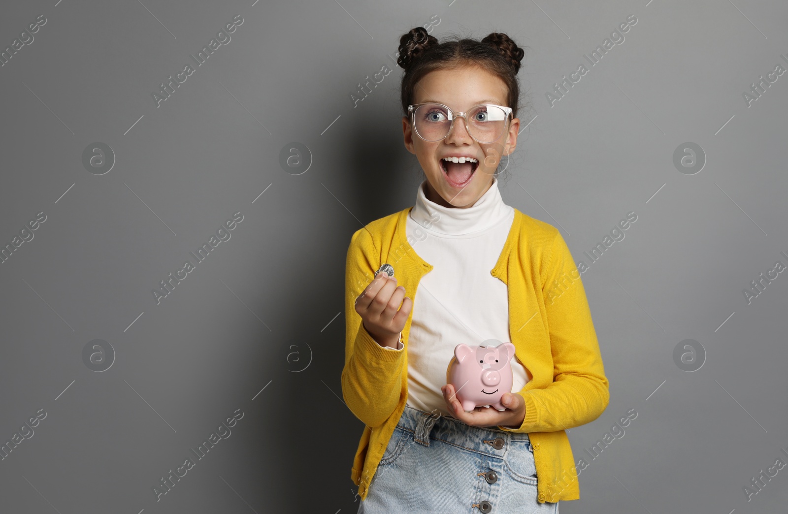 Photo of Pocket money. Cute girl with coins and piggy bank on grey background