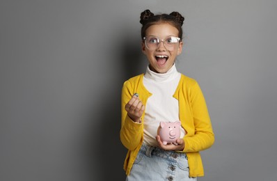 Pocket money. Cute girl with coins and piggy bank on grey background