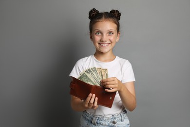 Photo of Pocket money. Cute girl with wallet and dollar banknotes on grey background