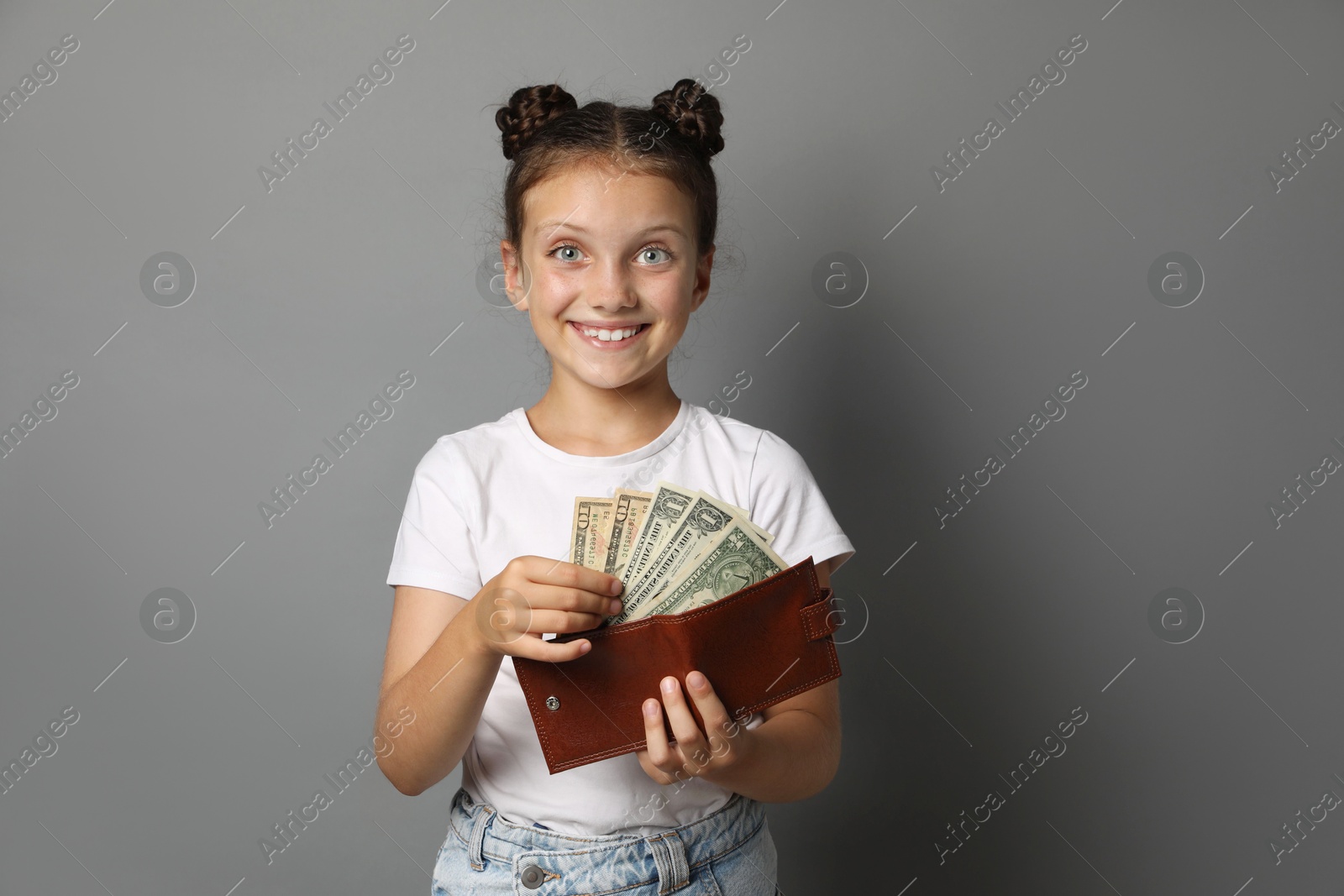 Photo of Pocket money. Cute girl with wallet and dollar banknotes on grey background