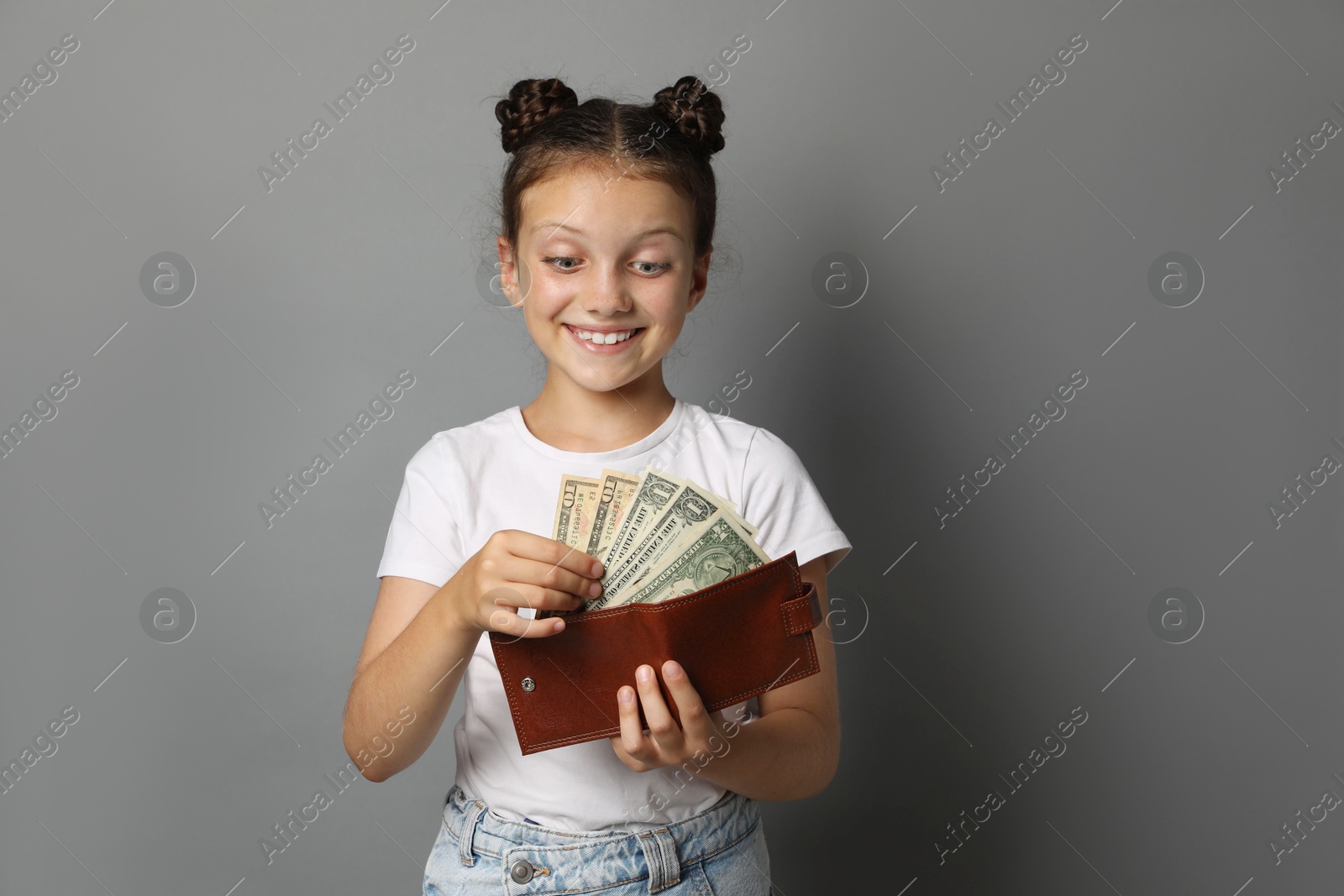 Photo of Pocket money. Cute girl with wallet and dollar banknotes on grey background