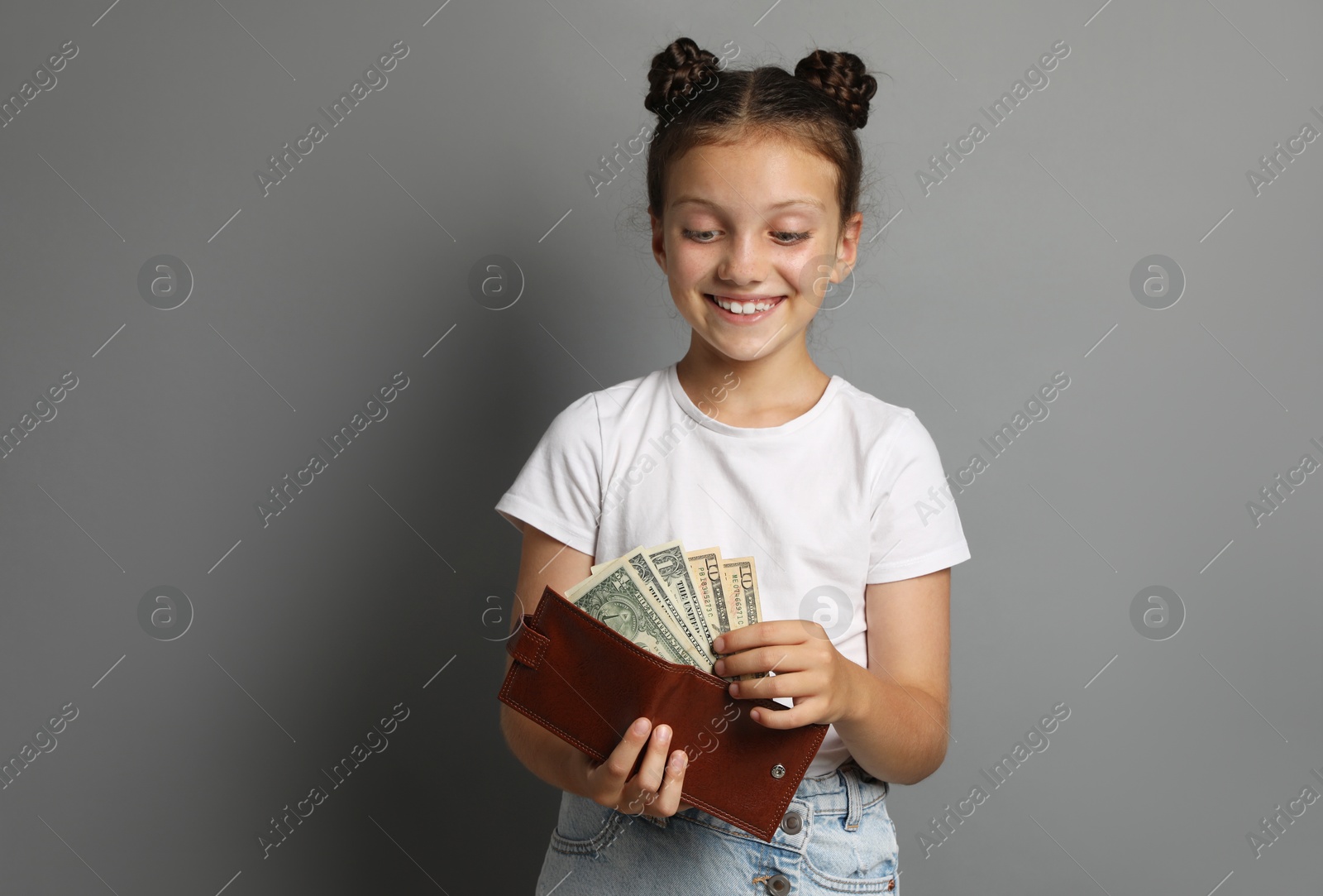 Photo of Pocket money. Cute girl with wallet and dollar banknotes on grey background