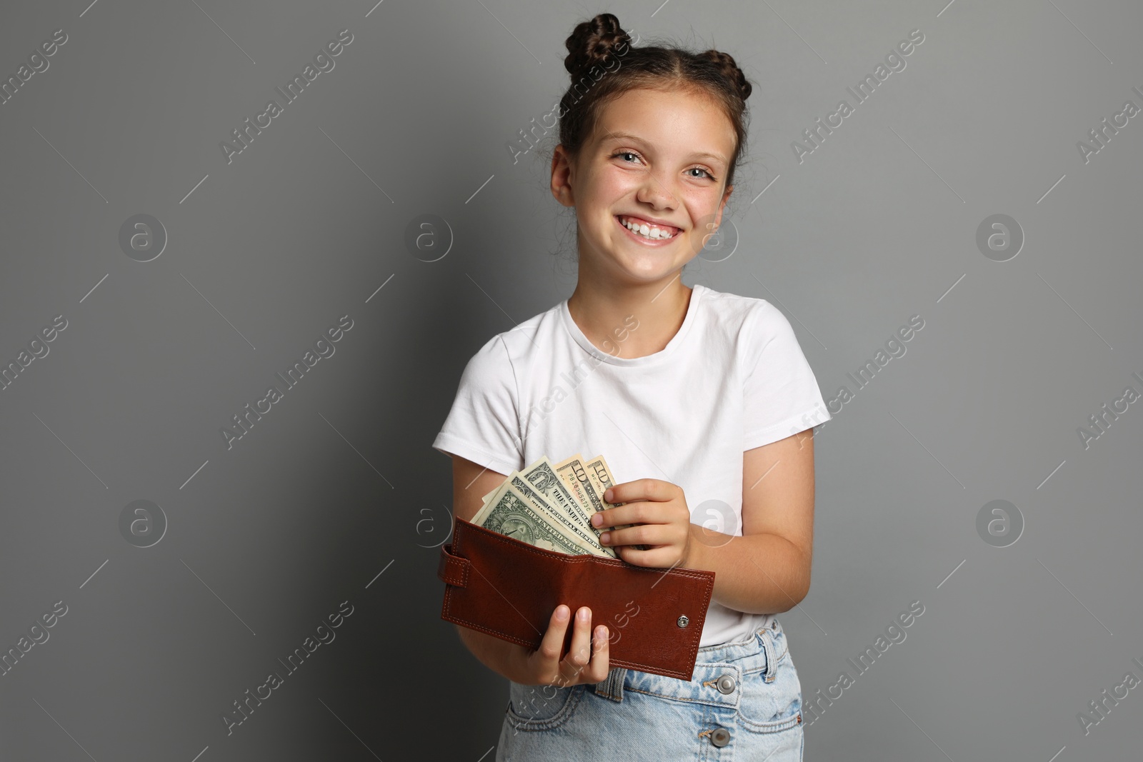 Photo of Pocket money. Cute girl with wallet and dollar banknotes on grey background