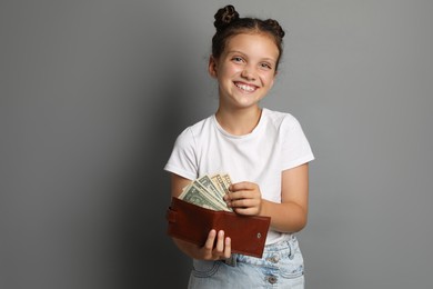 Pocket money. Cute girl with wallet and dollar banknotes on grey background