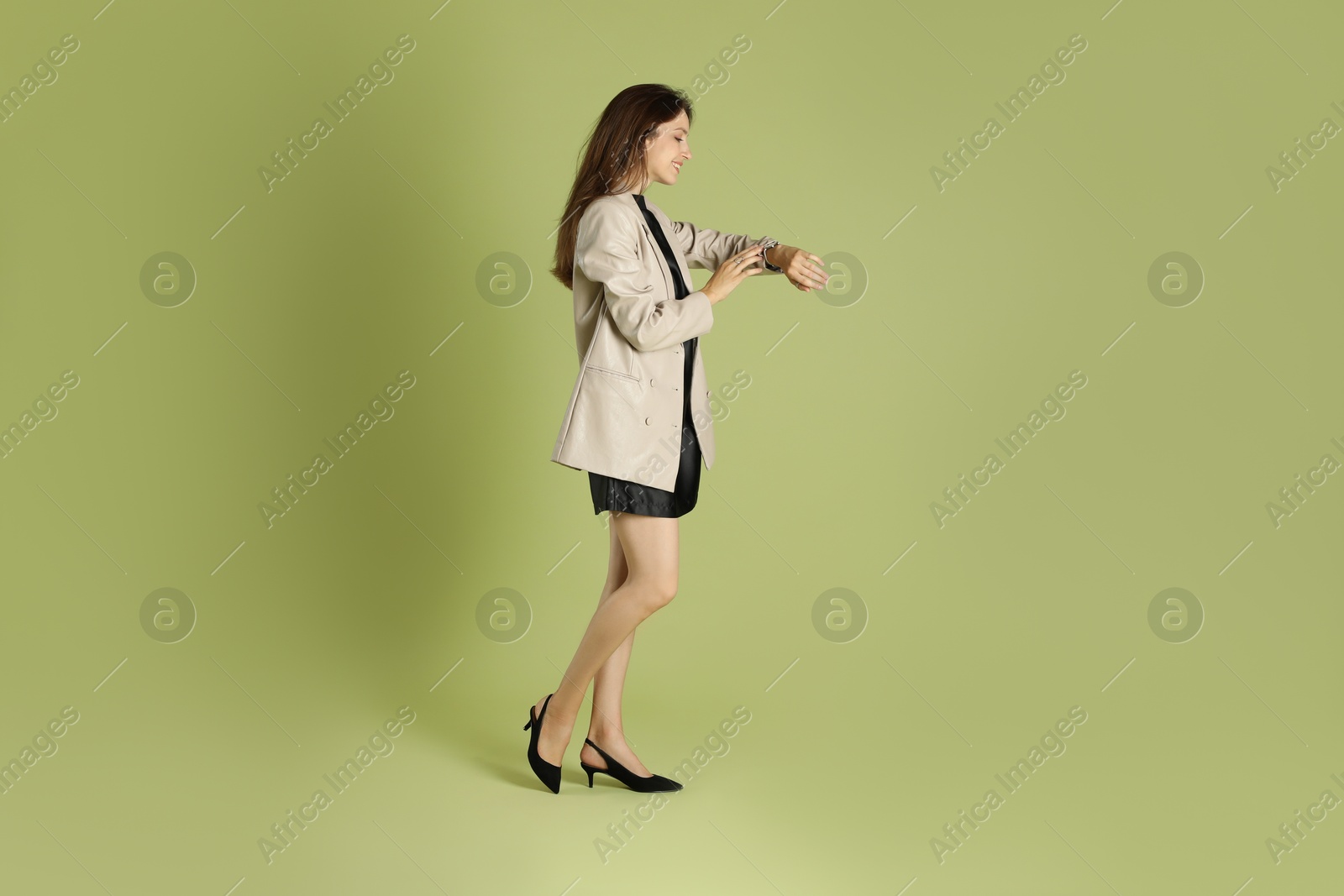 Photo of Beautiful woman in stylish beige jacket checking time on olive background