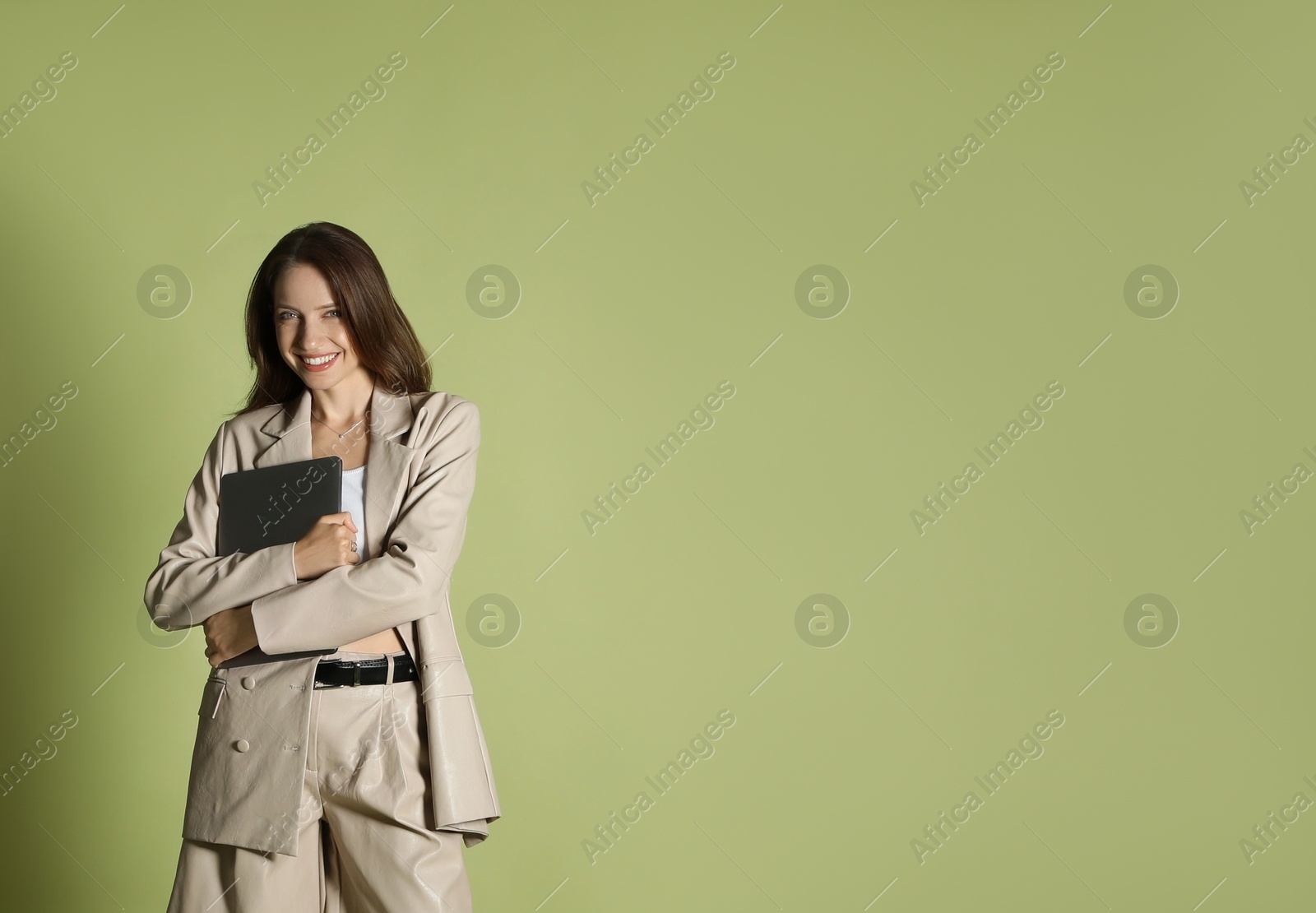 Photo of Beautiful woman in stylish beige suit with laptop on olive background, space for text