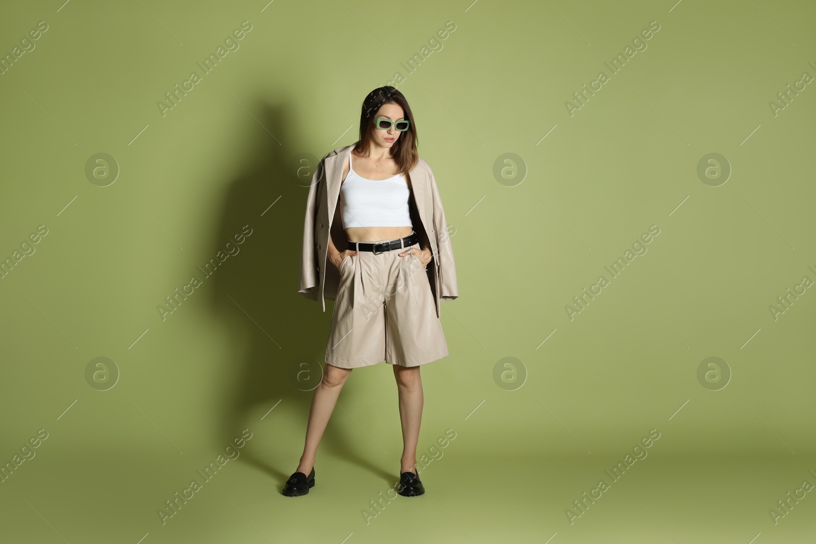 Photo of Beautiful woman in stylish beige suit and sunglasses on olive background, space for text