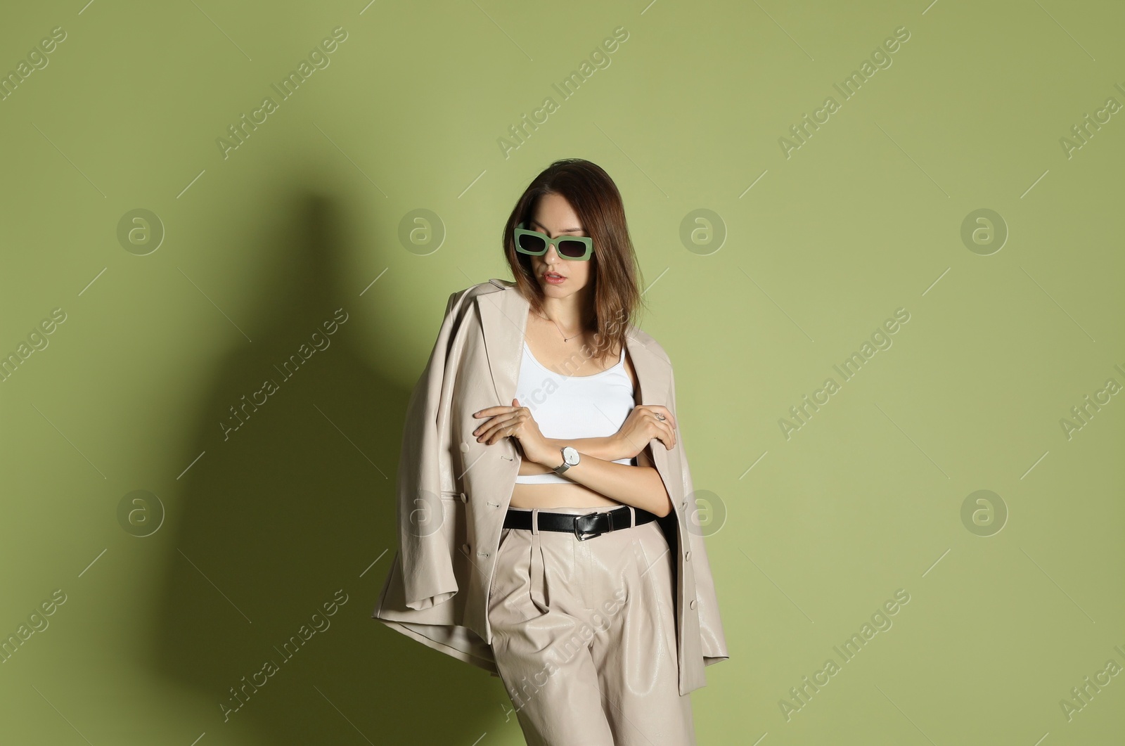 Photo of Beautiful woman in stylish beige suit and sunglasses on olive background