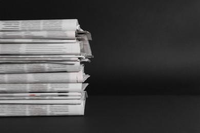 Stack of newspapers in different languages on black background. Space for text