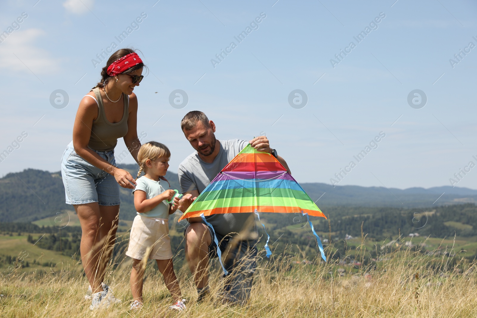 Photo of Family checking kite at field under blue sky. Space for text