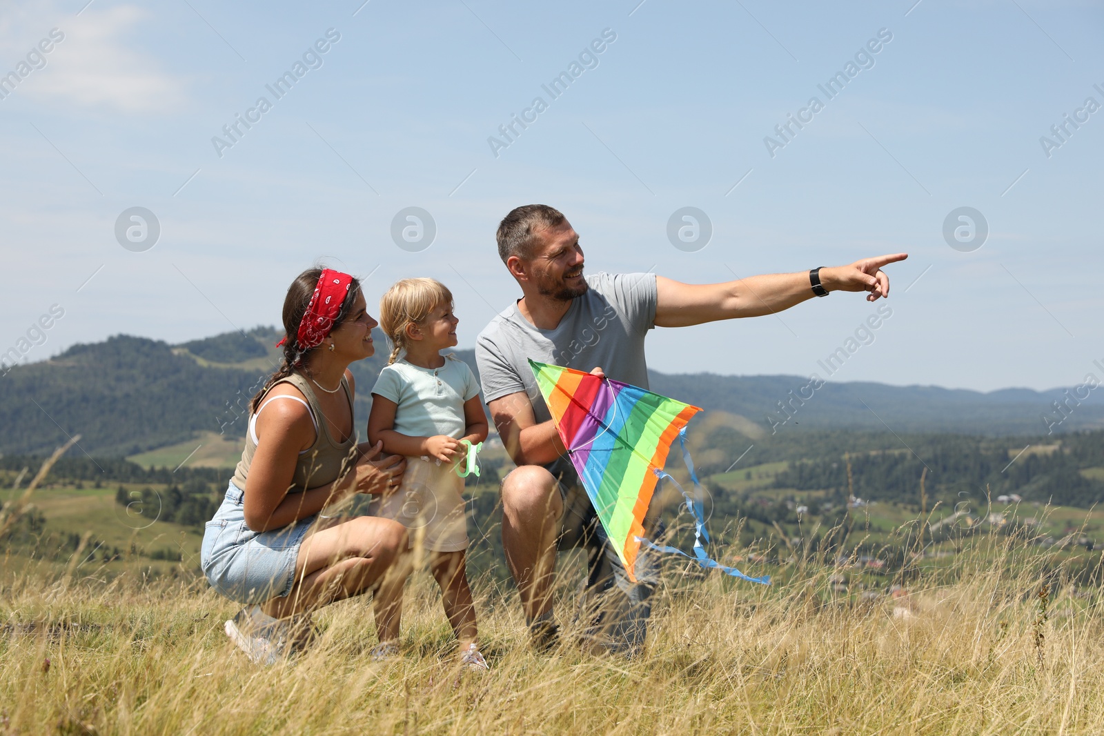 Photo of Smiling father with colorful kite pointing at something to his family at field