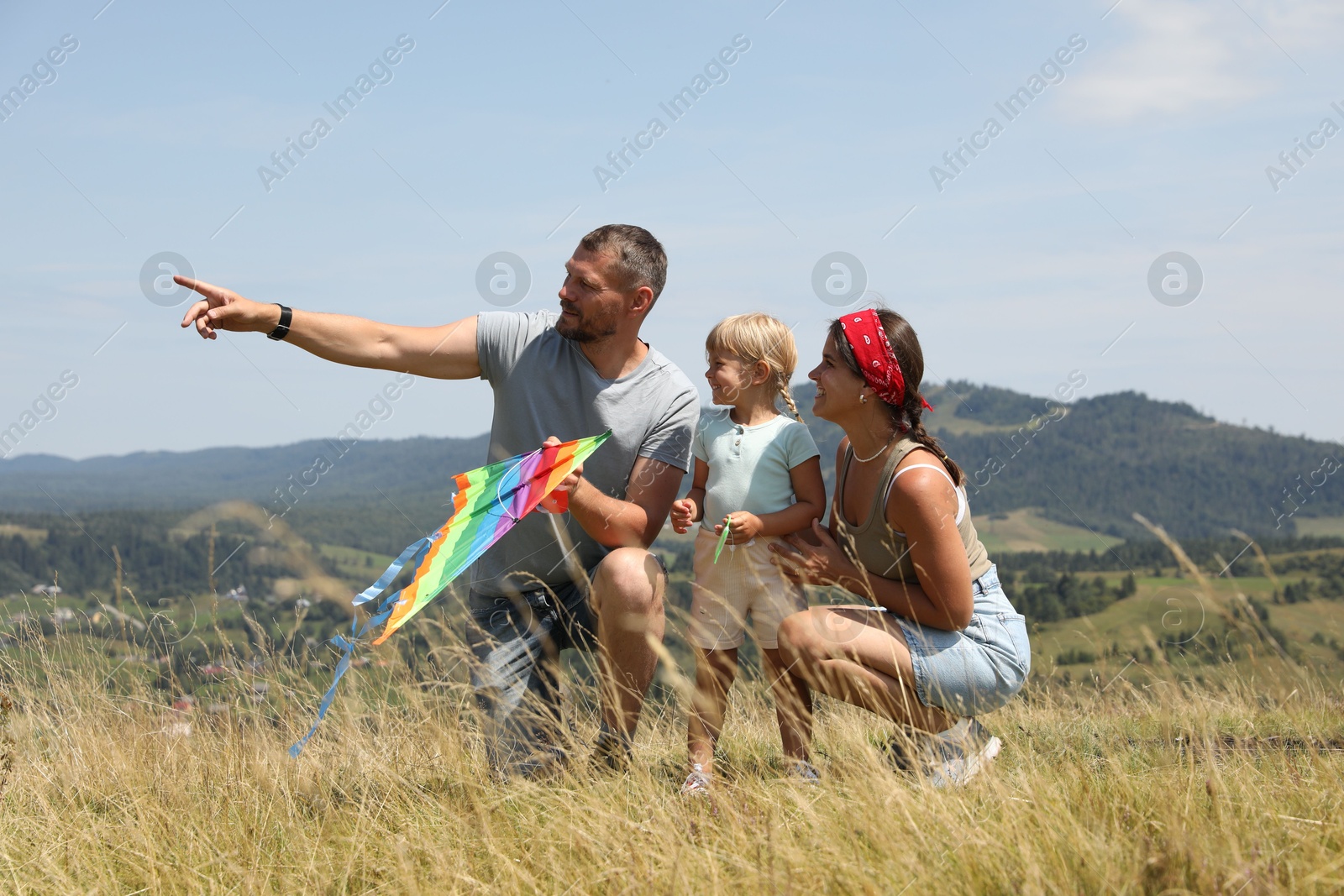 Photo of Father with colorful kite pointing at something to his family at field