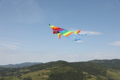 One colorful kite flying in mountains under blue sky